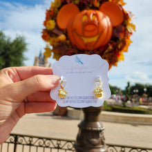 Load image into Gallery viewer, Gold pumpkin earrings held in front of a pumpkin and castle, with a blurred background
